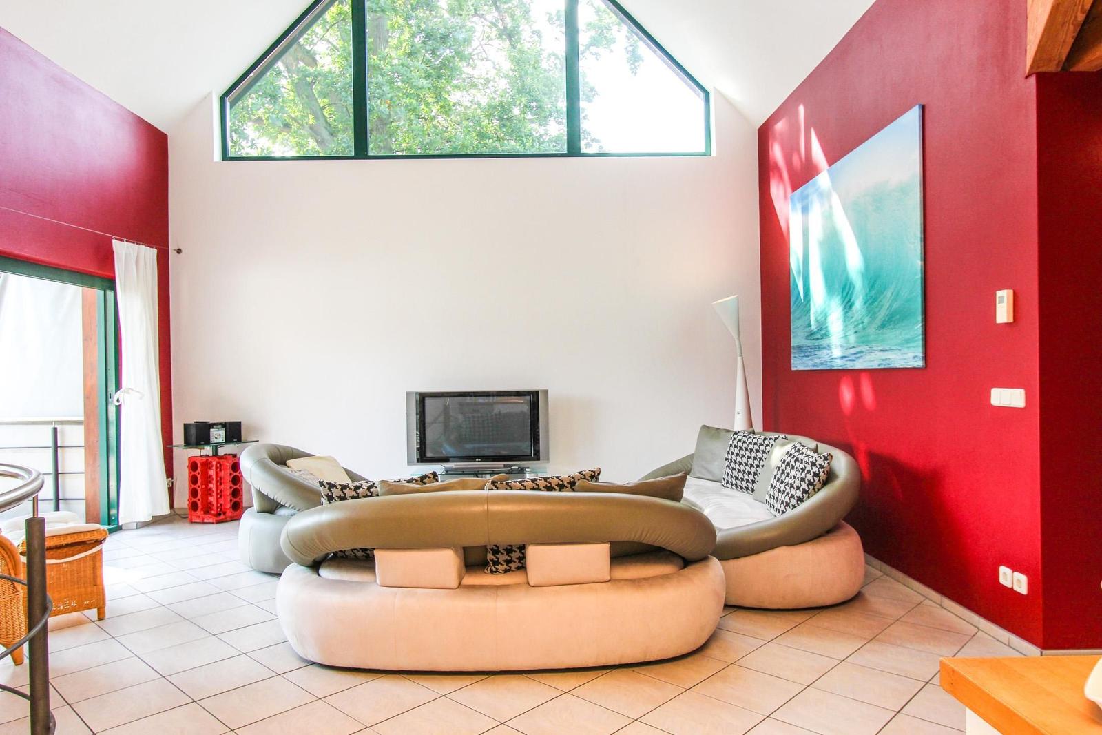 Wohnzimmer mit runden Sofas, roten Wänden und großem Fenster. Wandbild zeigt Wellen.