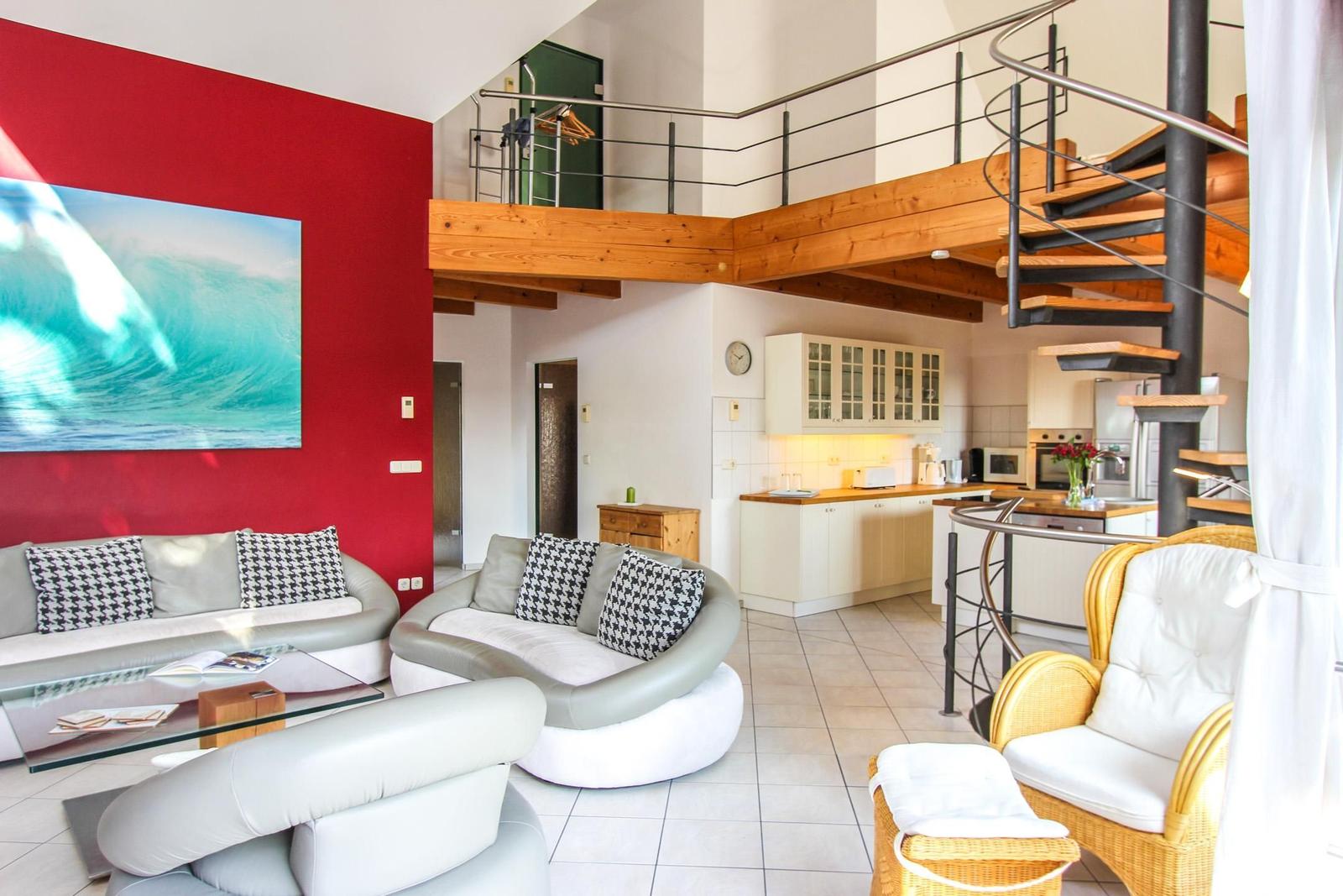 Wohnbereich mit roter Wand, Sofa, Couch und Küchenbereich mit Treppe.