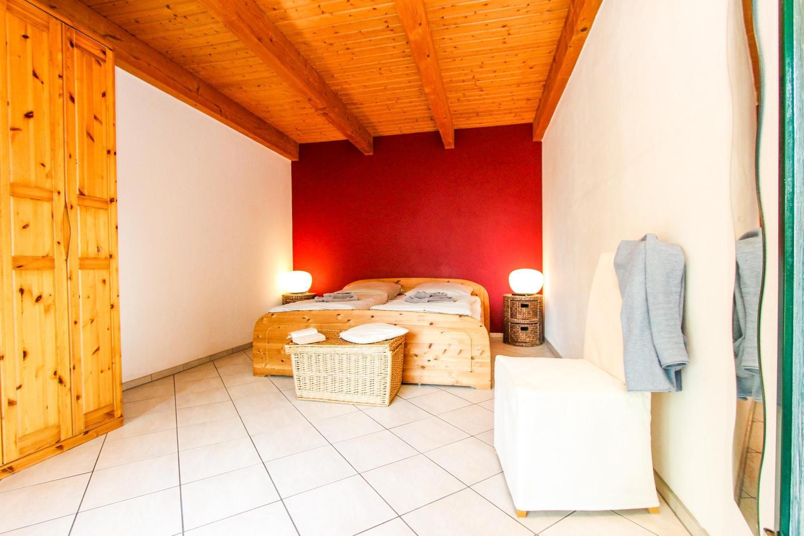 Schlafzimmer mit Holzbett, roter Wand, Körben und Holzboden.