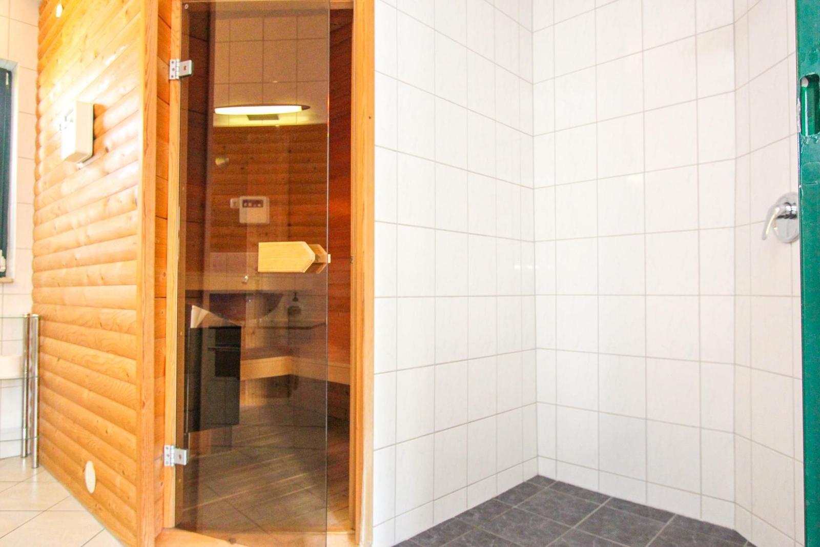 Sauna mit Holzwand und Glas Tür. Nebenraum mit weißen Fliesen und Dusche.