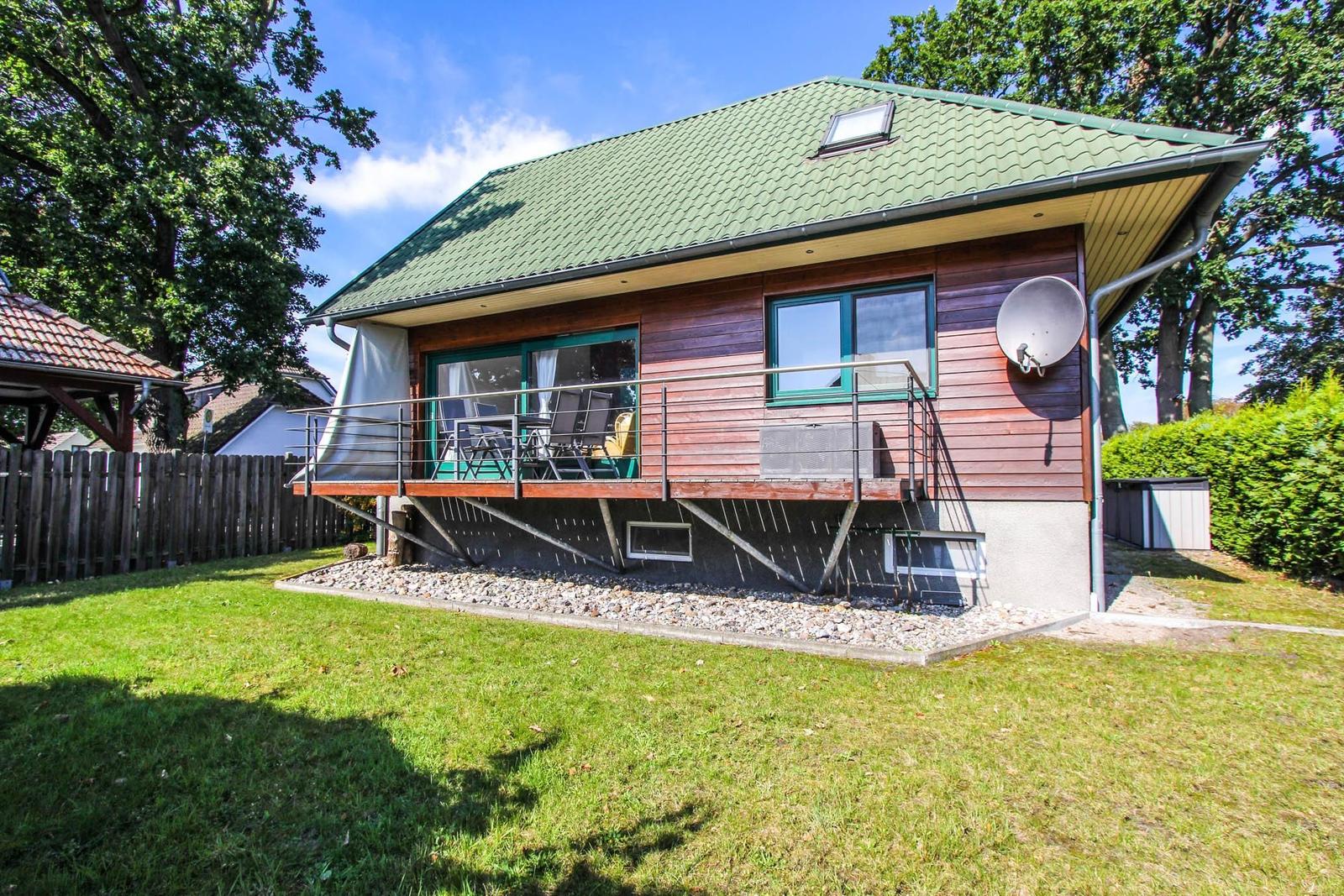 Ein Haus mit Balkon, grünem Dach und Holzfassade. Umgeben von Gras und Bäumen.