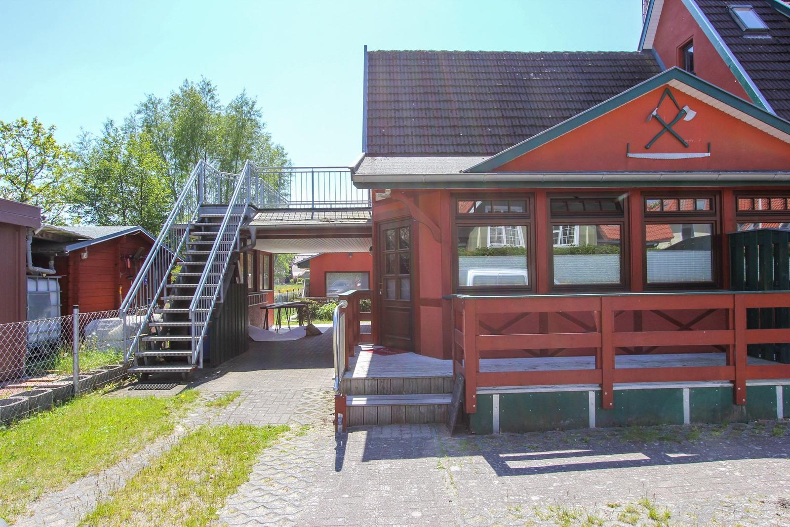 Rotes Ferienhaus mit Veranda, Treppe und Terrasse. Umgeben von Grün und Bäumen.