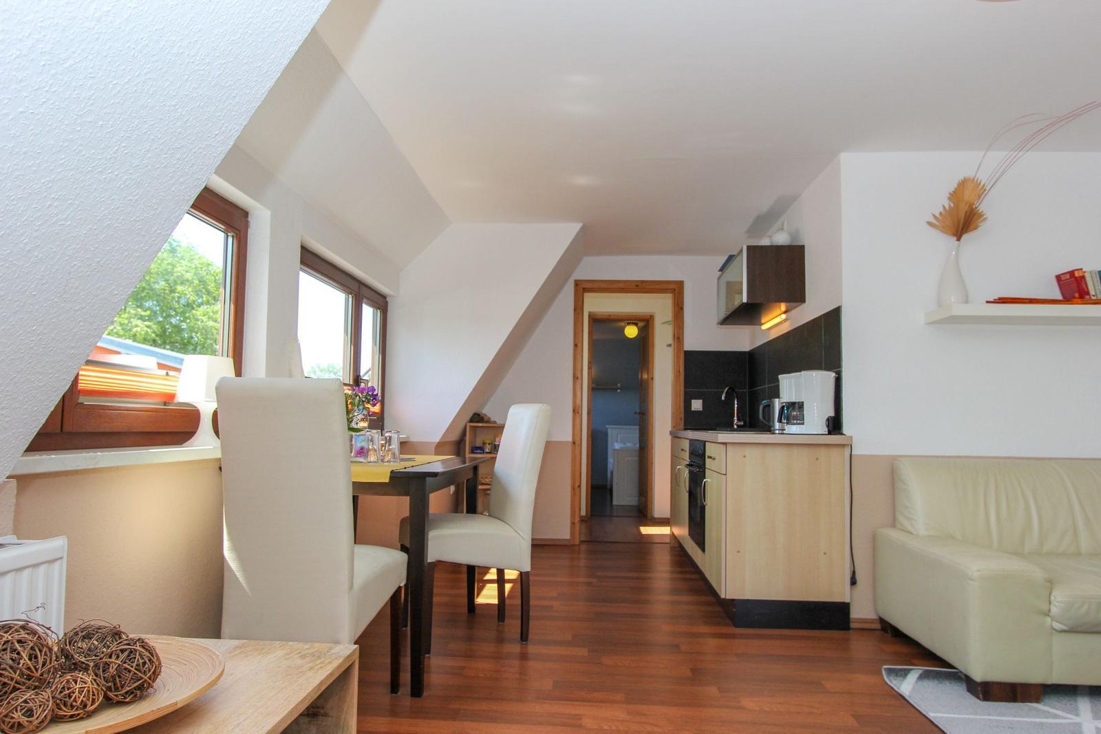 Wohnküche mit Essbereich, Sofa und Fenstern. Holzboden und Dachschrägen.