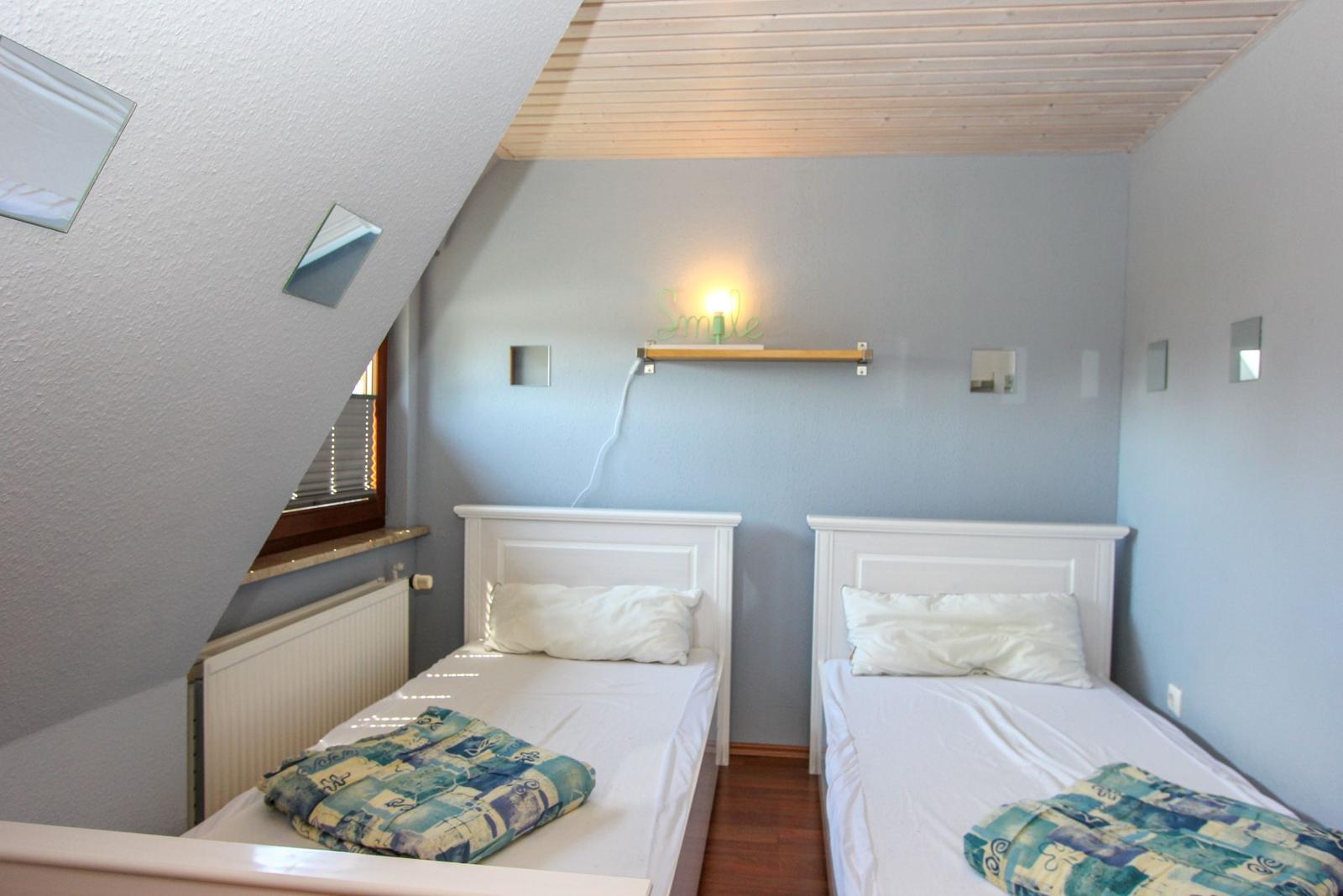 Zwei Einzelbetten in einem Dachzimmer mit Holzdecke und Wandspiegel.