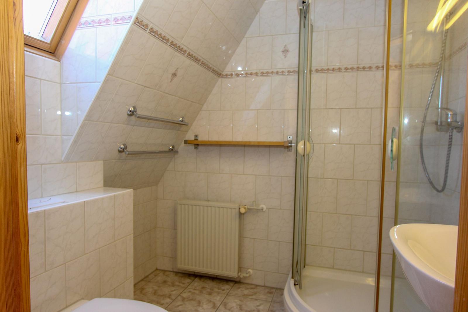 Badezimmer mit Dusche, Waschbecken und Dachfenster. Wandverkleidung und Bodenfliesen.