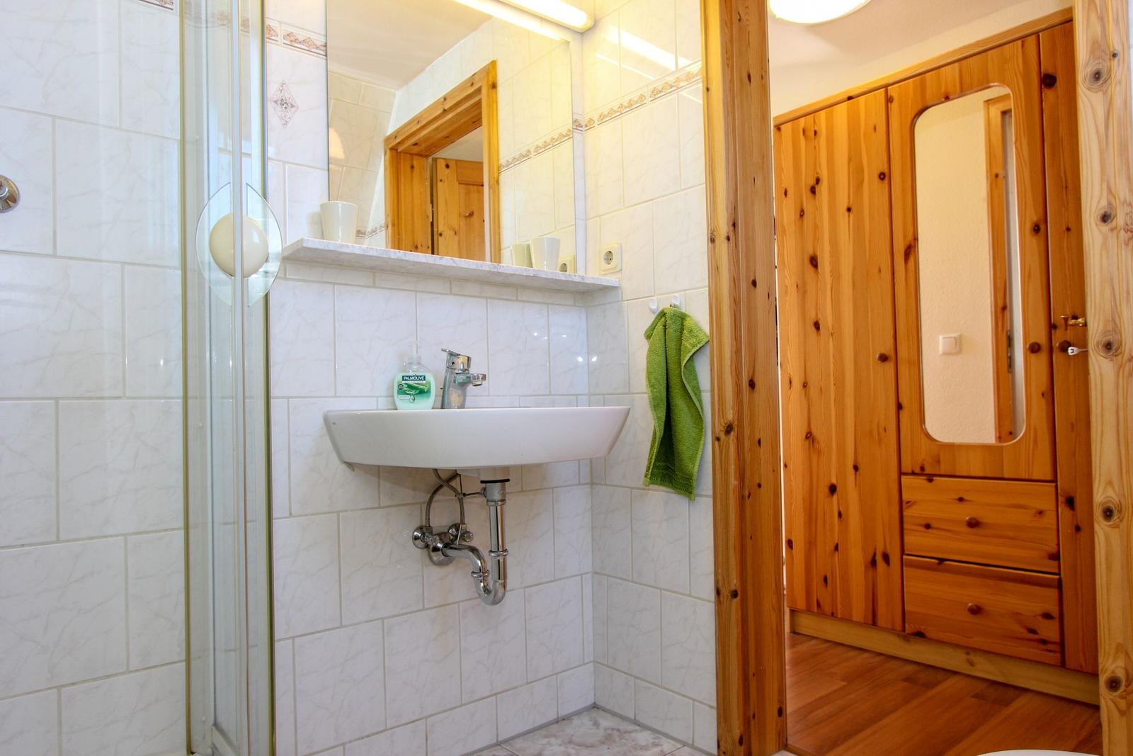 Badezimmer mit Dusche, Waschbecken und Holzschrank.