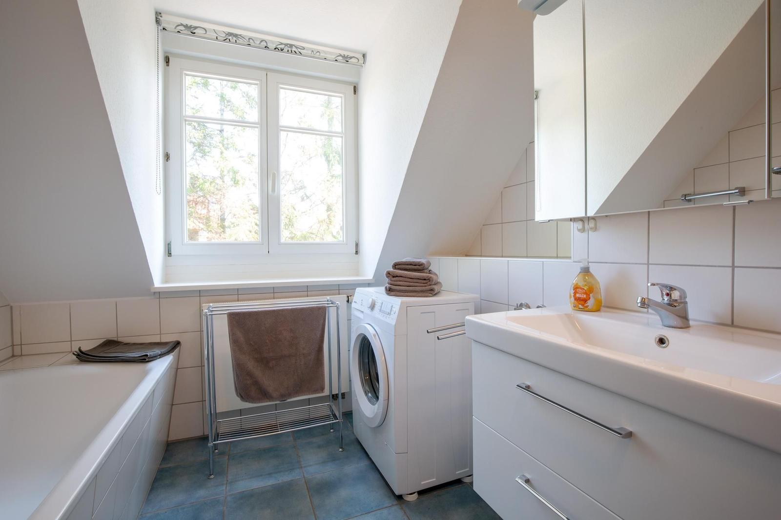 Badezimmer mit Waschmaschine, Badewanne und Waschtisch unter Dachschrägen.