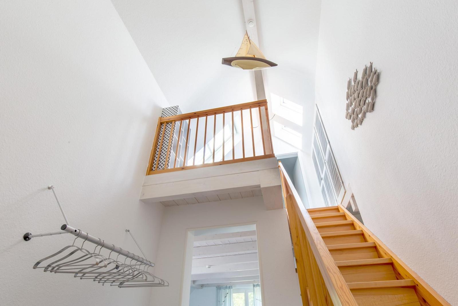 Haus mit Holztreppe, Balkon und Hängeschrank. Deckenleuchte und Wanddekoration sichtbar.