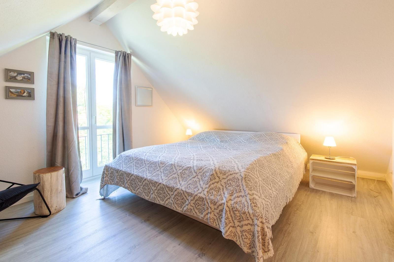 Schlafzimmer mit Dachschräge, Bett, Fenster, Nachttische und Deckenleuchte.