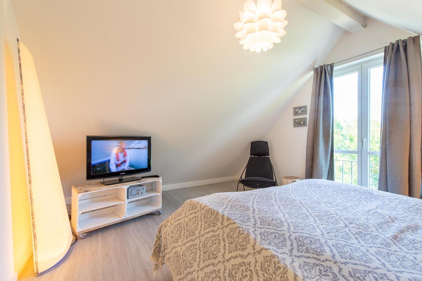 Schlafzimmer mit Bett, Fernseher und Fenster zur Terrasse.