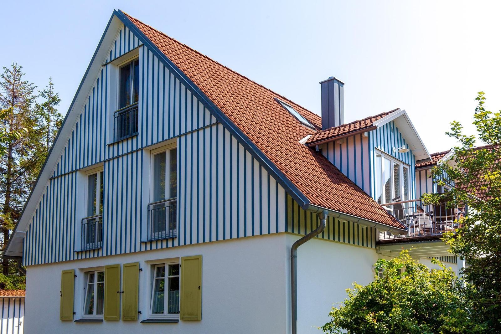 Haus mit blau-weißem Streifenfassade, rotem Dach und grünen Fensterläden.
