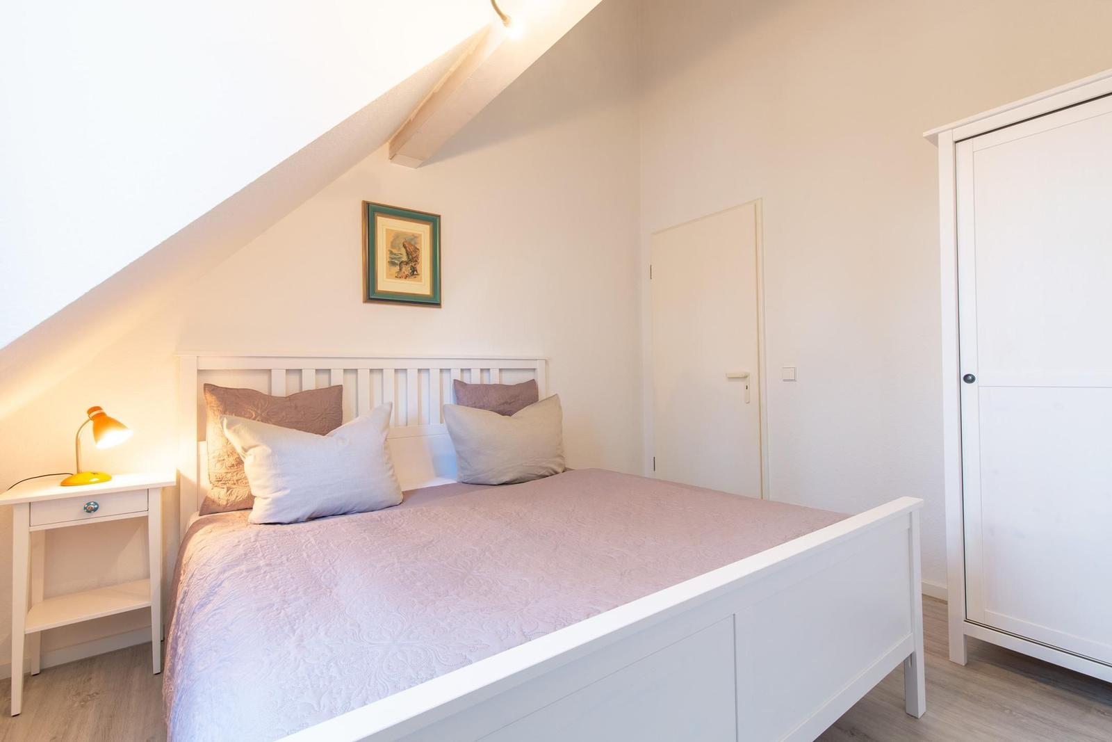 Schlafzimmer mit weißem Bett, Nachttisch und Kleiderschrank unter Dachschrägen.