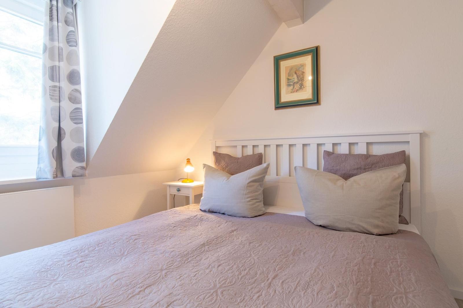 Schlafzimmer mit Bett, Nachttisch und Fenster unter Dachschrägen.