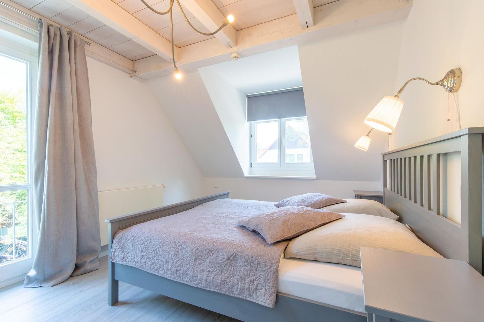 Schlafzimmer mit Doppelbett, Fenster und Holzbalkendecke.