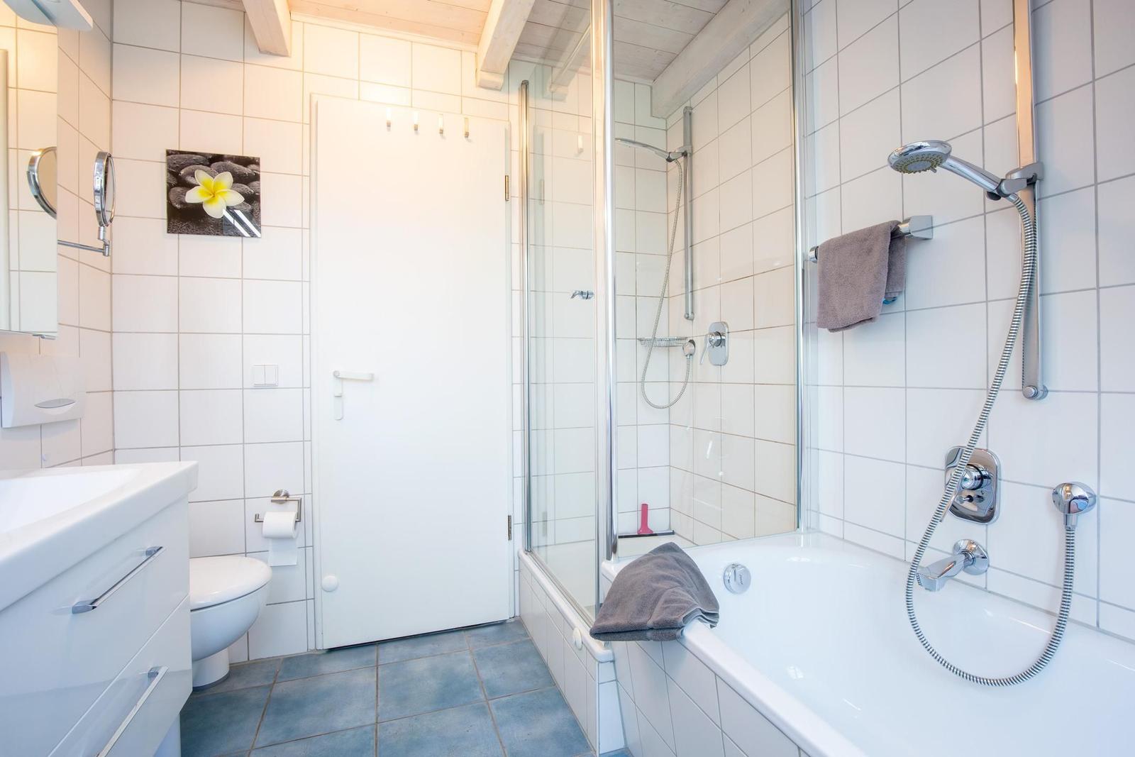 Badezimmer mit Dusche, Badewanne und Toilette. Weiße Fliesen und Holzbalken an der Decke.