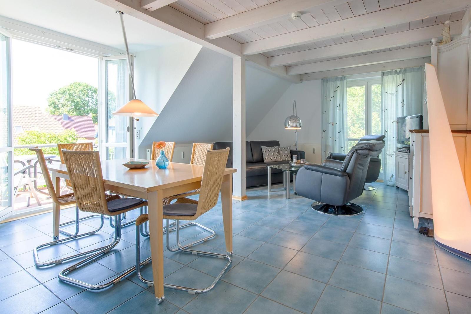 Essbereich mit Tisch und Stühlen. Wohnbereich mit Sofa und Sessel. Große Fenster und Terrasse.