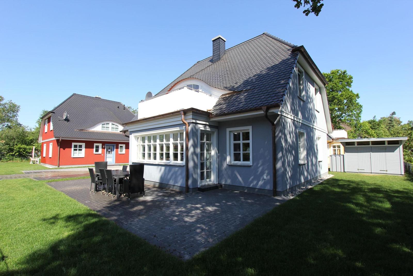 Haus mit Terrasse, Garten und Grillplatz. Nebenhaus und Garage sind sichtbar.