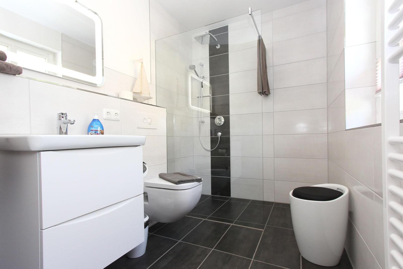 Badezimmer mit Dusche, Waschbecken und Toilette. Fliesenboden und Spiegel.