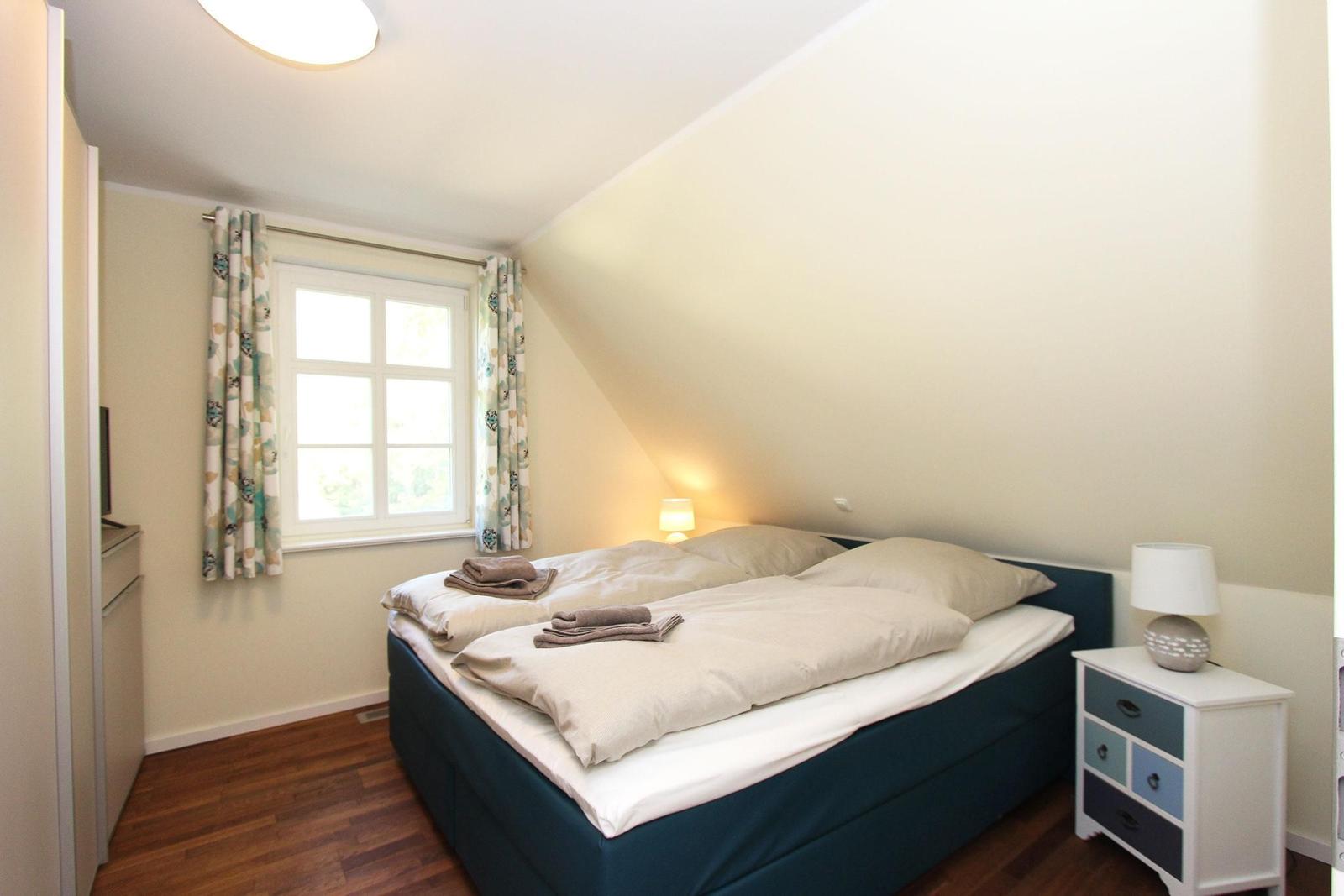 Schlafzimmer mit Doppelbett, Fenster und Nachttisch.