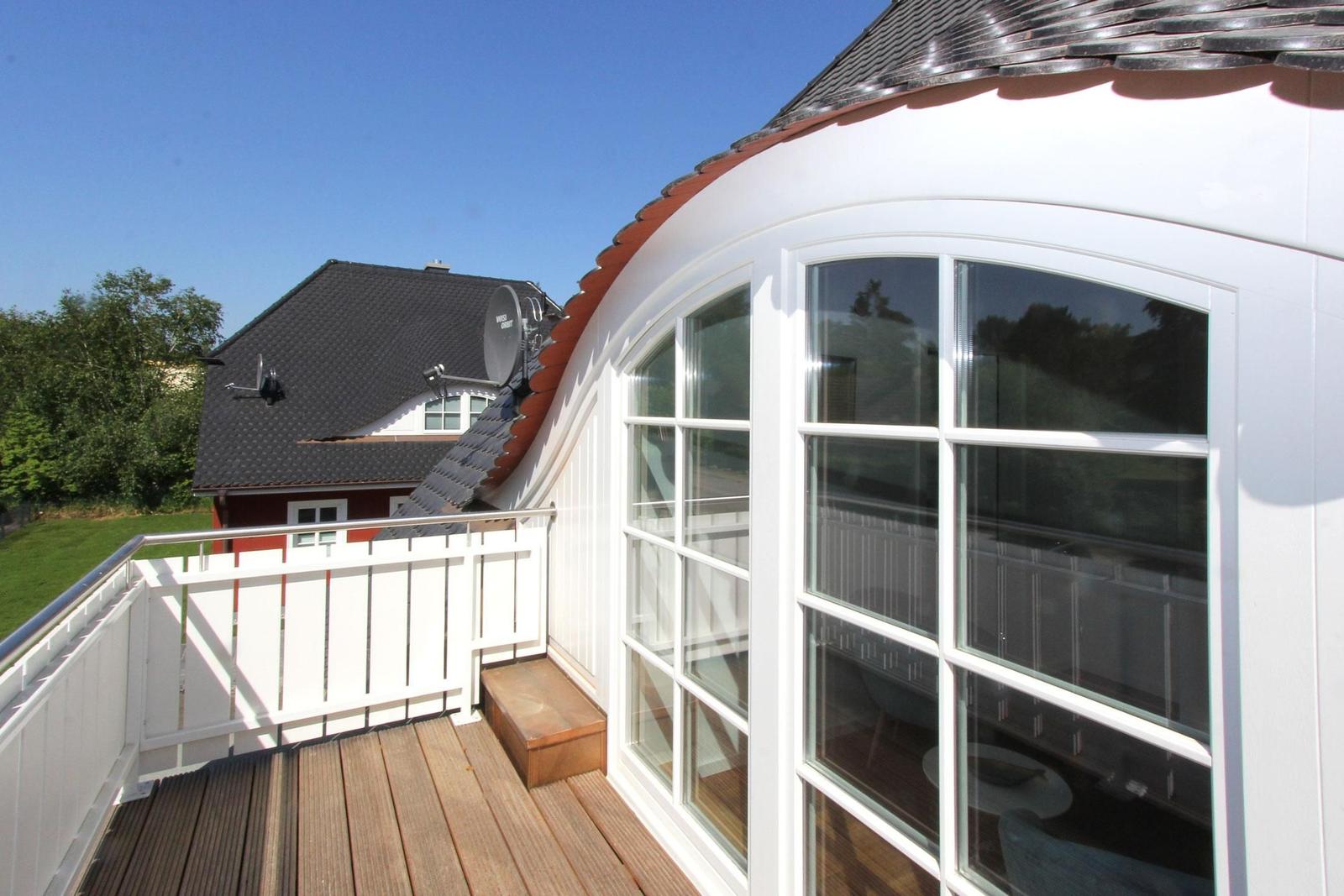 Terrasse mit Holzboden und weißer Brüstung. Blick auf ein Haus mit Satellitenschüssel.
