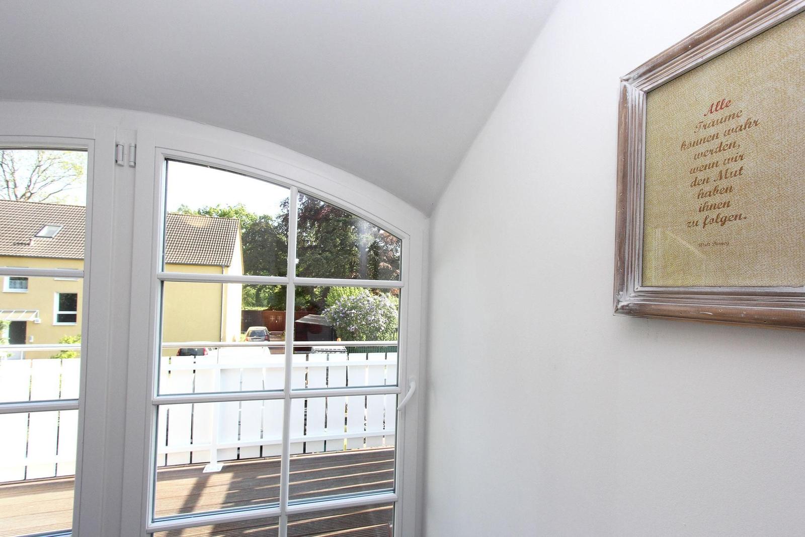 Blick durch Bogenfenster auf Balkon mit weißem Geländer und Garten