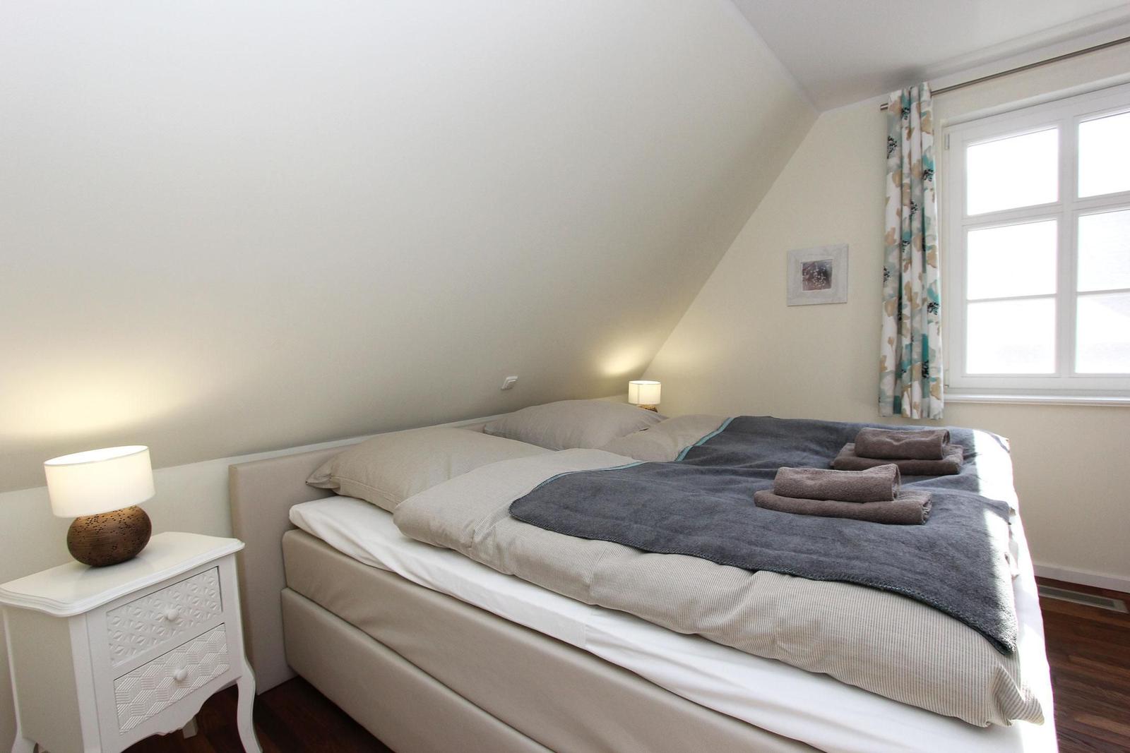 Schlafzimmer mit Doppelbett, Nachttisch und Fenster mit Vorhängen.
