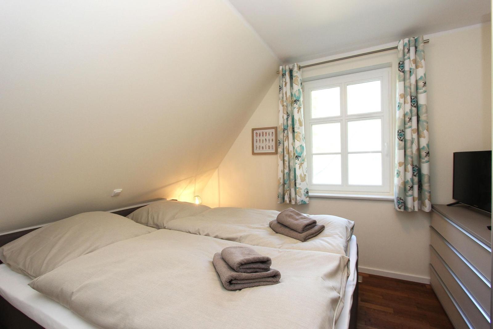 Schlafzimmer mit Doppelbett, Fenster und TV.