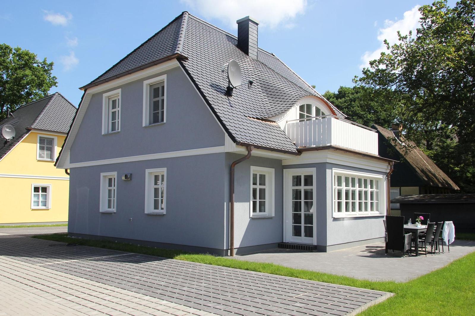 Ein graues Haus mit weißen Fenstern und einem Balkon. Außenterrasse mit Tisch und Stühlen.
