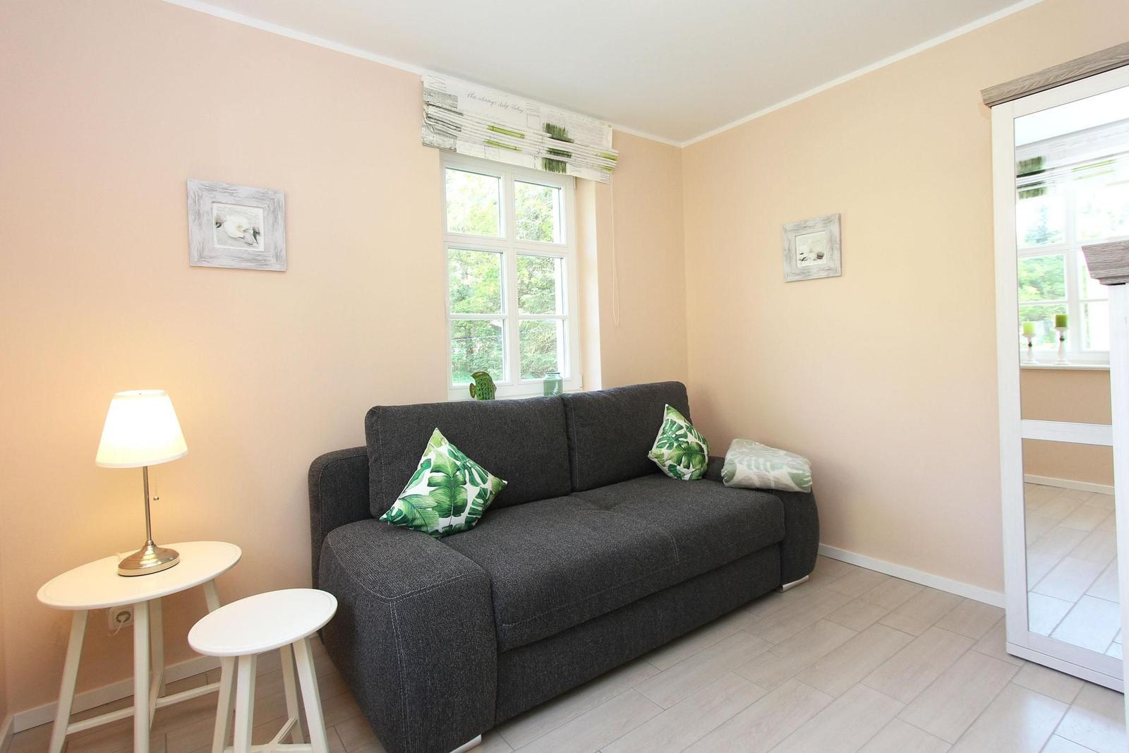 Ein Wohnzimmer mit grauem Sofa, grünen Kissen und einem Fenster mit Blick nach draußen.