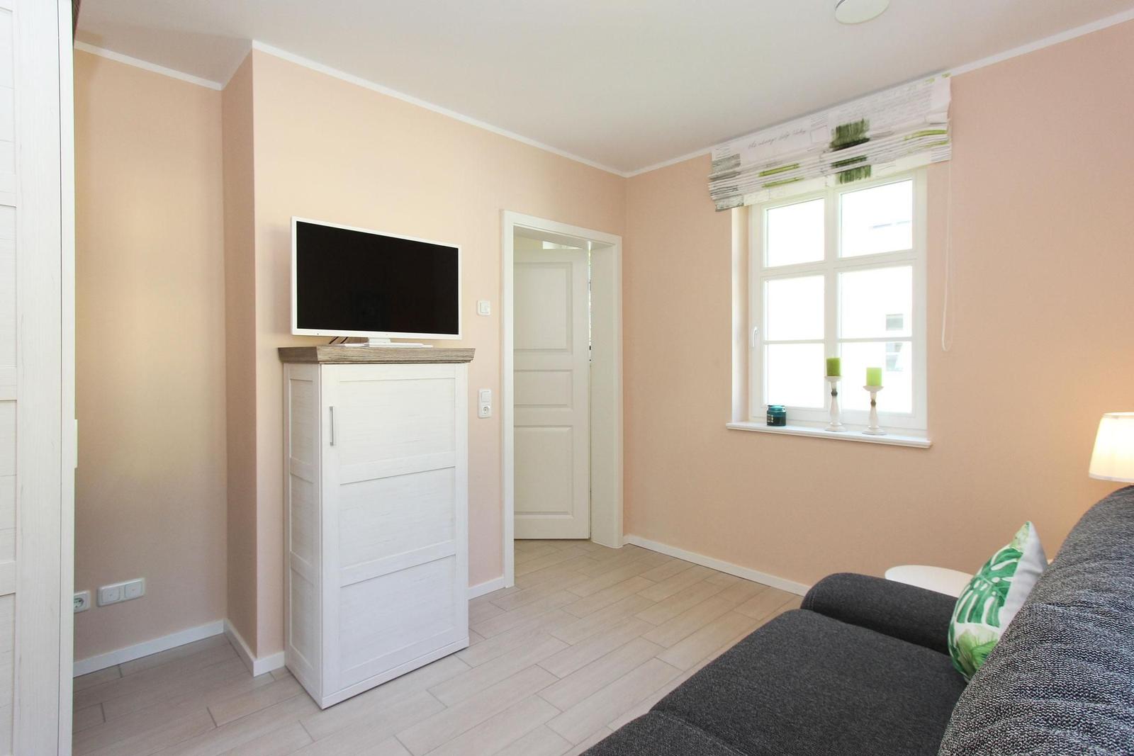 Wohnzimmer mit Sofa, TV und Fenster. Wandfarbe rosa, Holzboden.