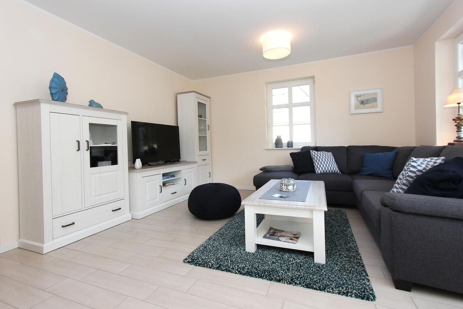 Wohnzimmer mit grauem Sofa, weißem Couchtisch und Fernseher auf Möbeln.