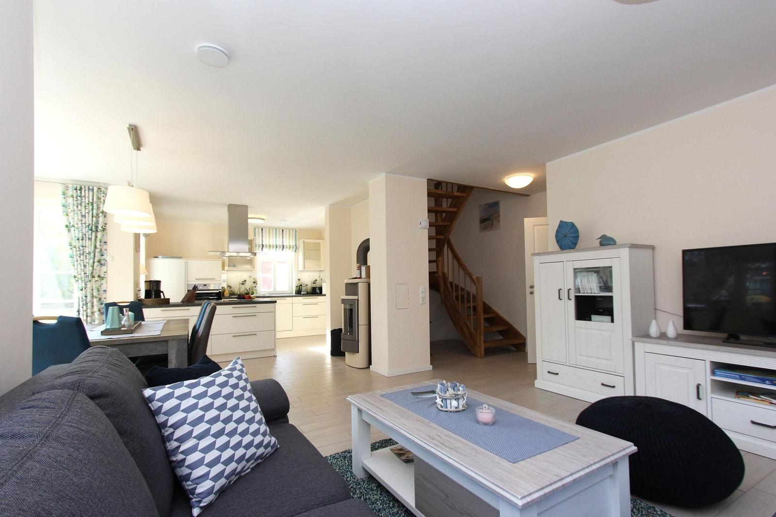 Wohnbereich mit Sofa, Couchtisch und TV. Küche und Treppe sind sichtbar.