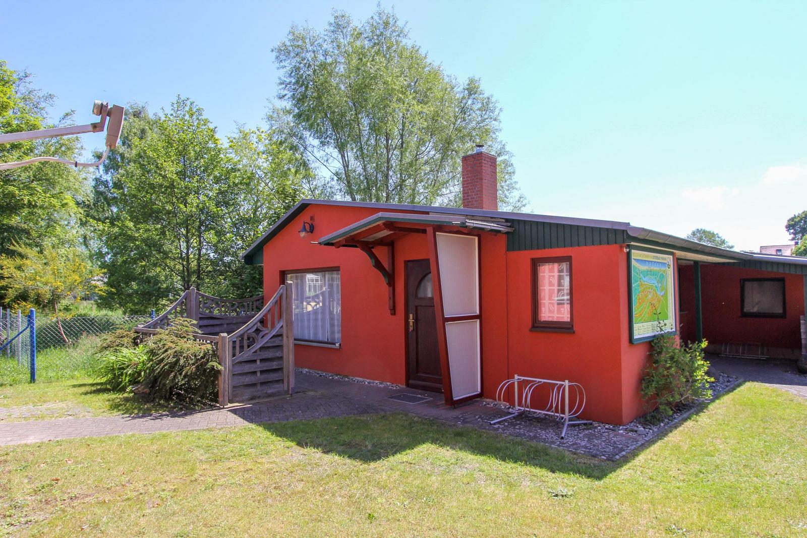 Rotes Ferienhaus mit Eingangstreppe, Fahrradständer und Garten. Holzterrasse und Kamin.