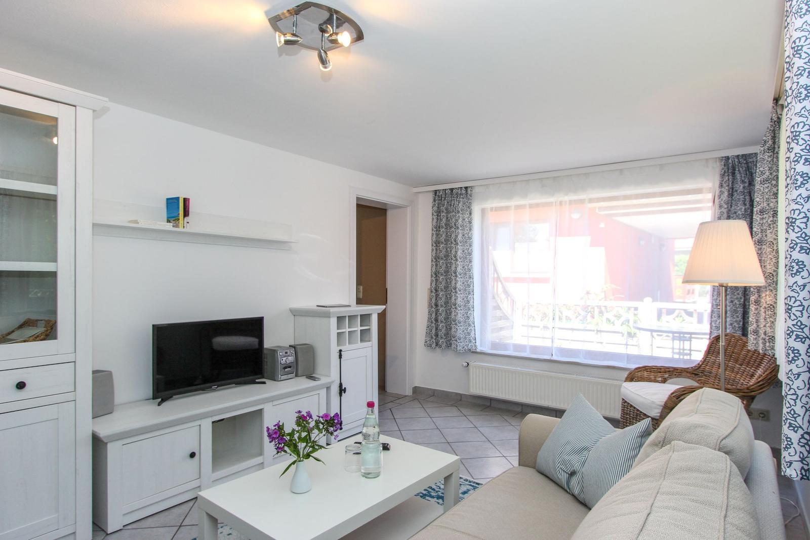 Wohnzimmer mit Sofa, Fernseher und Tisch. Fenster mit Blick auf Balkon.