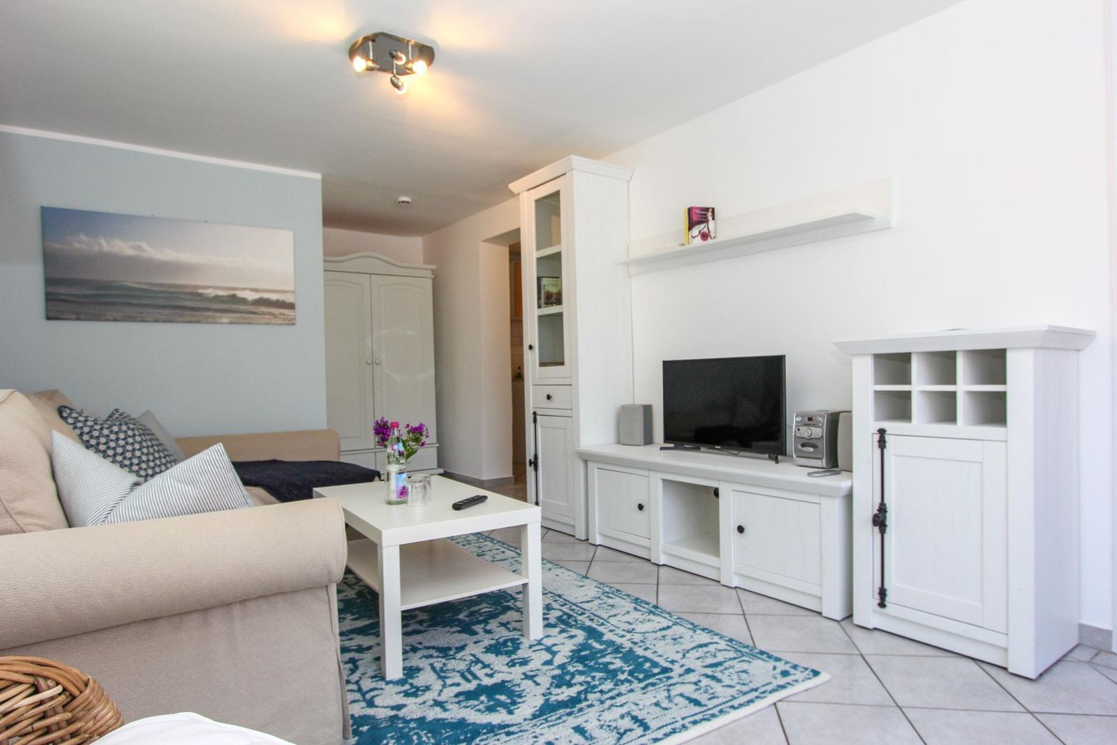 Wohnzimmer mit Sofa, TV und weißen Schränken auf hellen Fliesen.