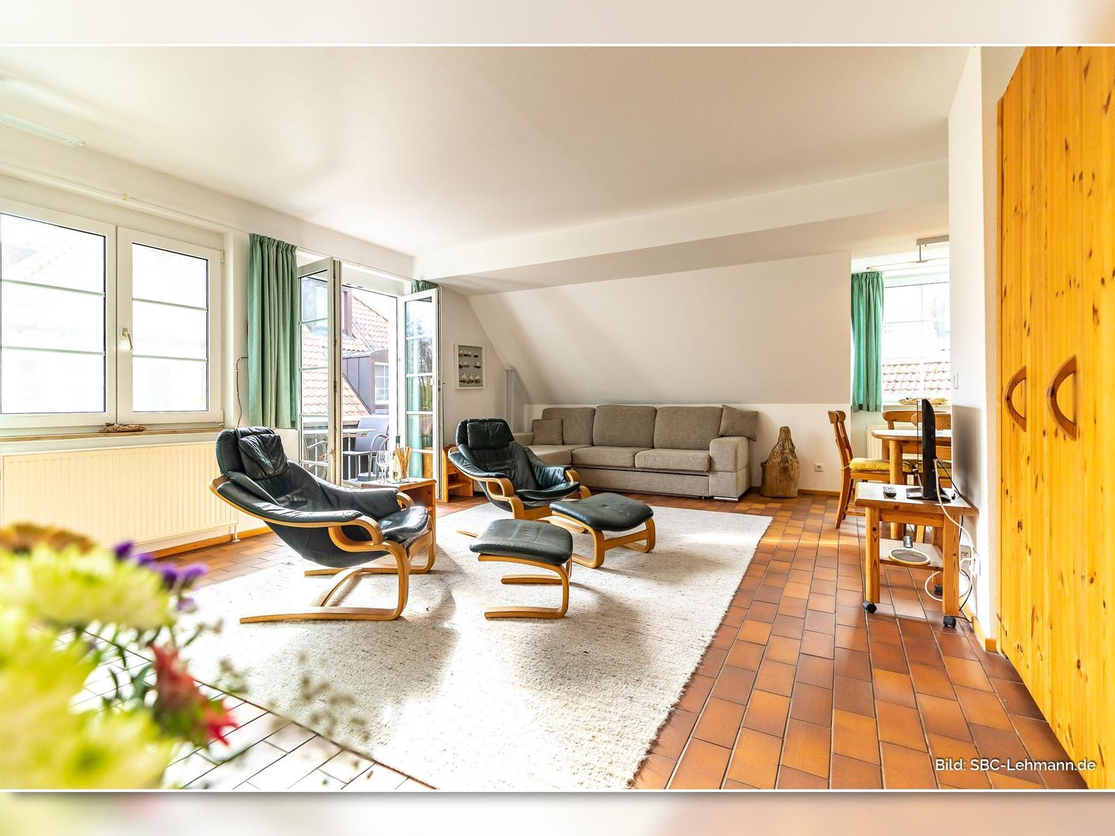 Wohnzimmer mit zwei schwarzen Sesseln, Sofa und Terrassentür.