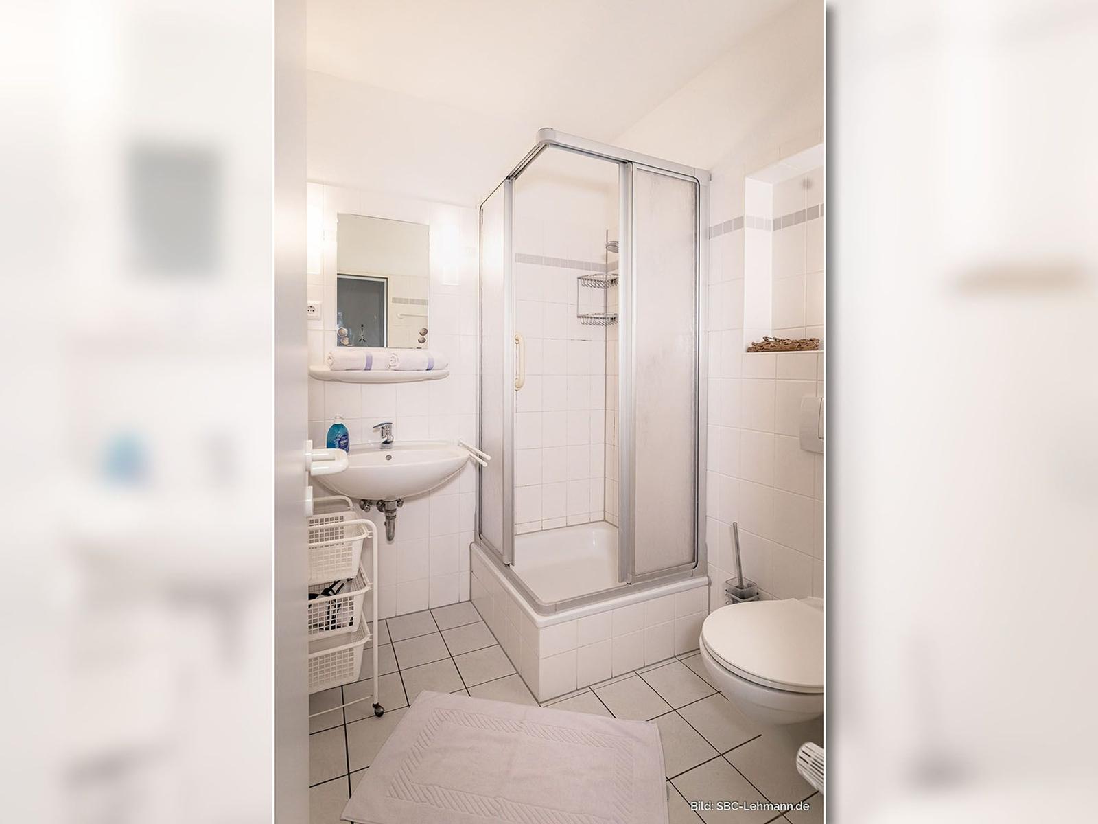 Badezimmer mit Dusche, Waschbecken und Toilette. Fliesenboden und Spiegelschrank.
