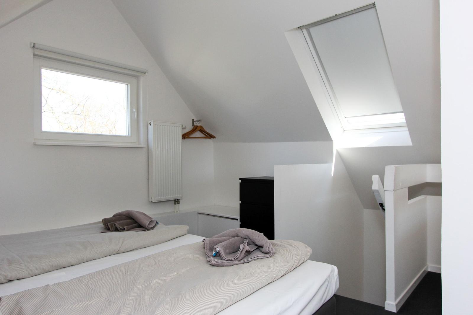 Schlafzimmer mit Dachschrägen, Fenster und Dachfenster. Bett, Kleiderschrank und Heizkörper.