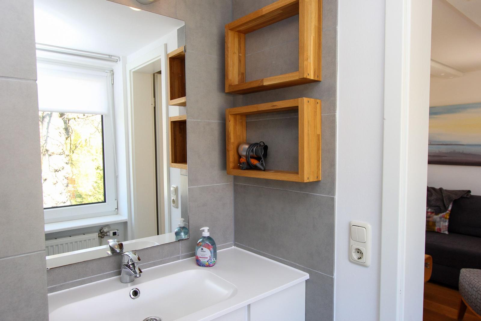 Badezimmer mit Waschbecken, Spiegel und Holzregalen an der Wand.