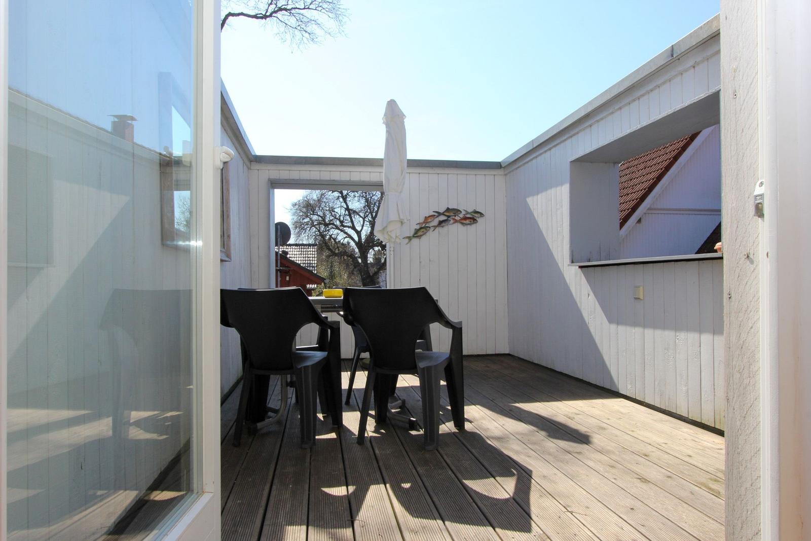 Terrasse mit Tisch, Stühlen und geschlossenem Sonnenschirm. Holzdecke und weiße Wände.