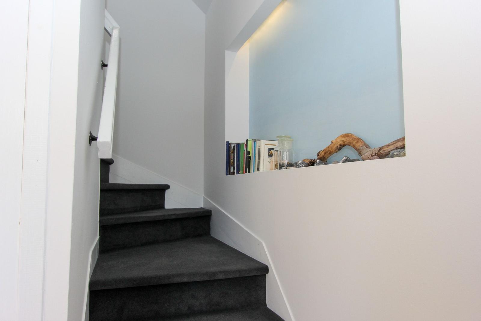 Treppenhaus mit dunkelgrauen Stufen und einer Wandnische mit Büchern und Holzstücken.