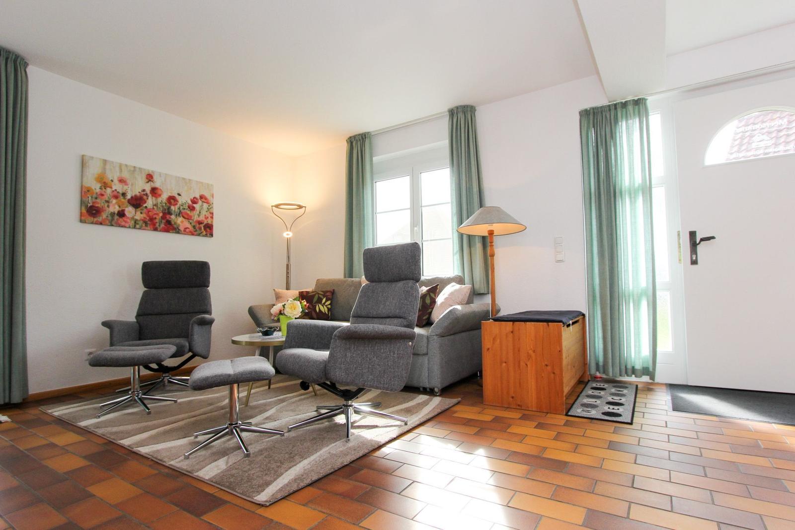 Wohnzimmer mit Sofa, zwei Sessel und Holzfußboden. Fenster mit grünen Vorhängen.