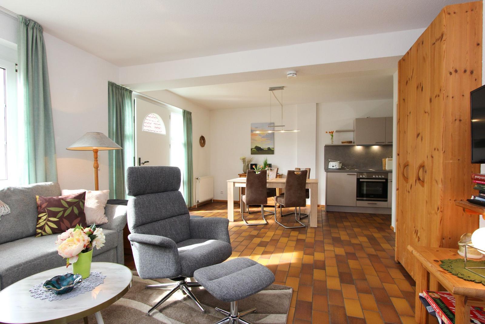 Wohnbereich mit Sofa, Sessel und Essbereich. Küche mit Ofen und Holzschränken.