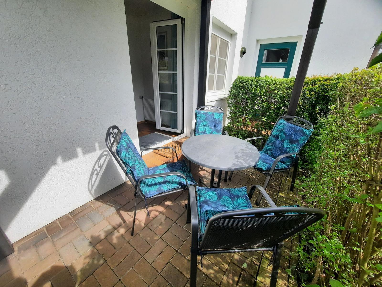 Terrasse mit runden Tisch und vier Stühlen mit blauen Kissen.
