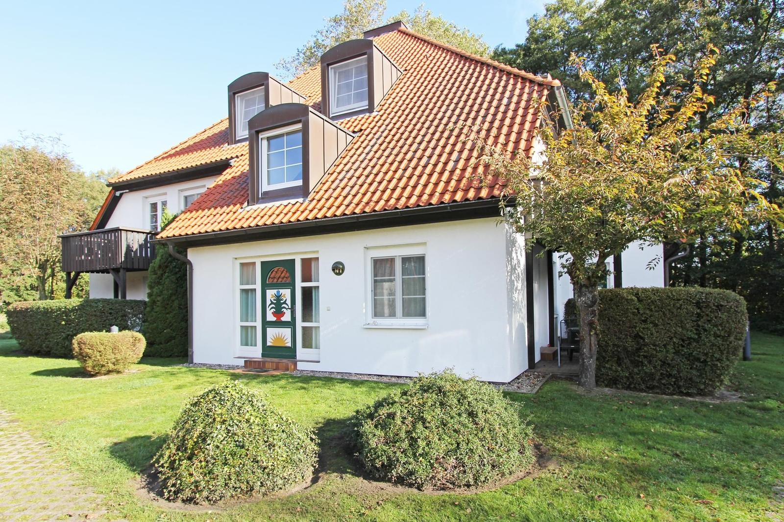 Ein weißes Haus mit rotem Ziegeldach und grüner Haustür im Garten.