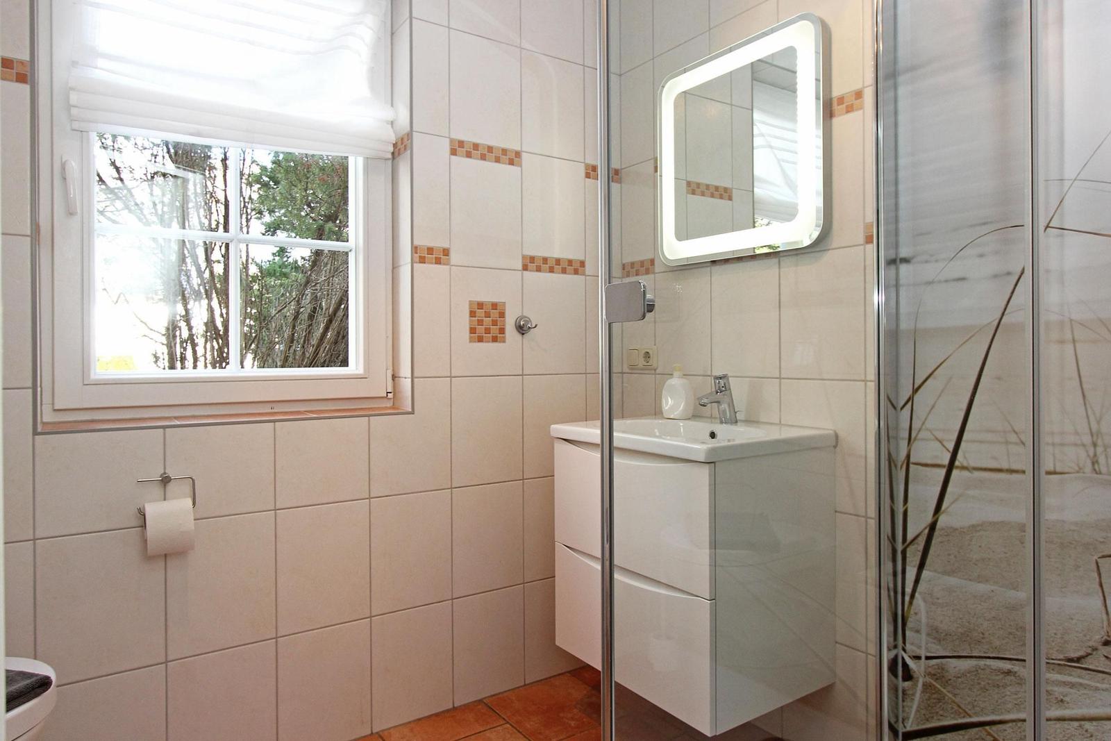 Badezimmer mit Dusche, Waschbecken und Fenster mit Blick auf Bäume.