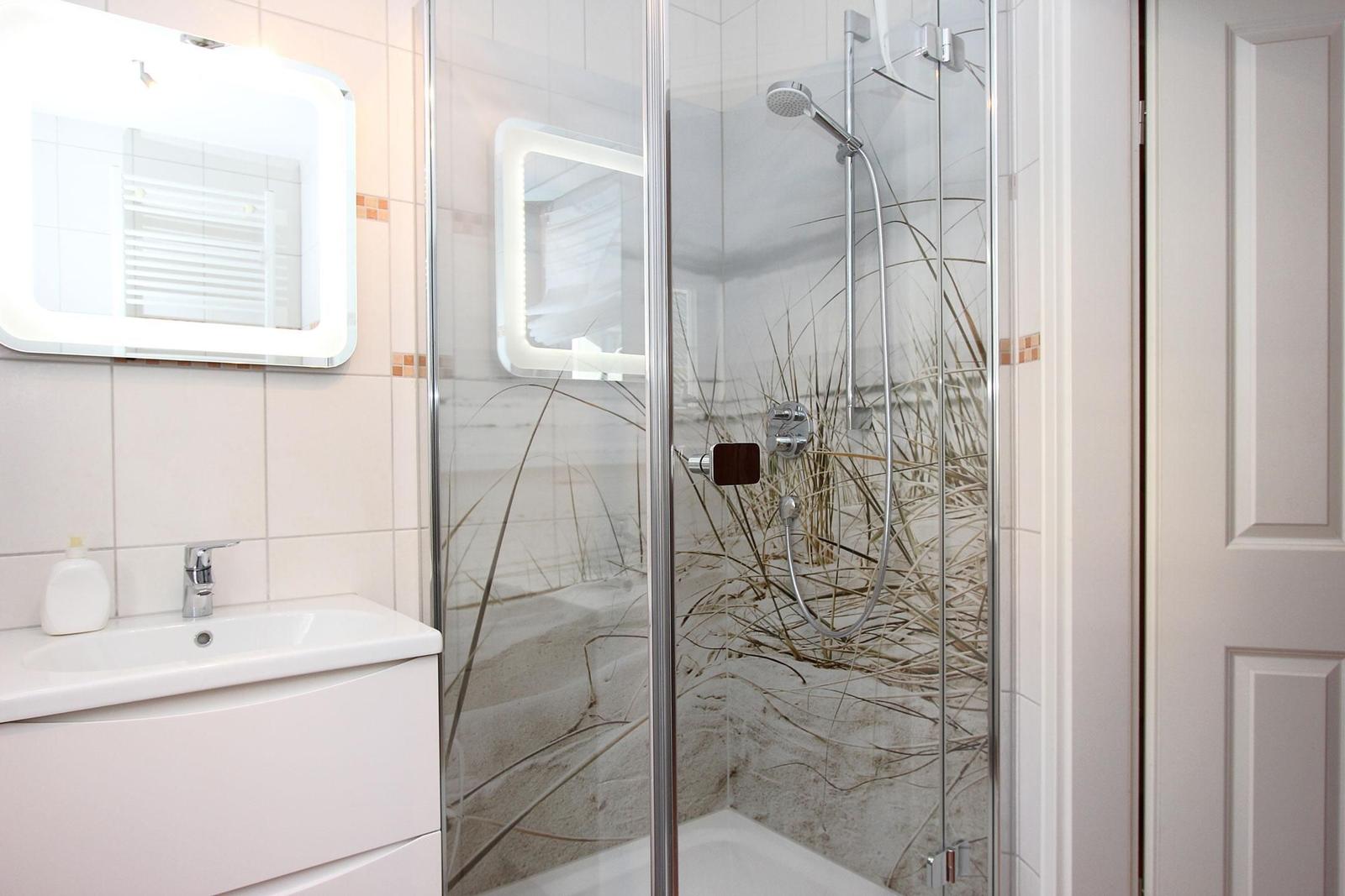 Badezimmer mit Dusche und Waschbecken. Duschwand hat Strandmotiv.
