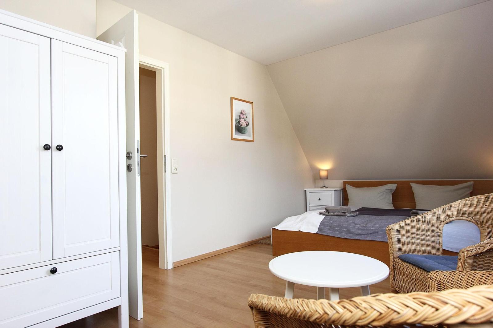 Schlafzimmer mit Bett, Kleiderschrank und Sitzgelegenheit.