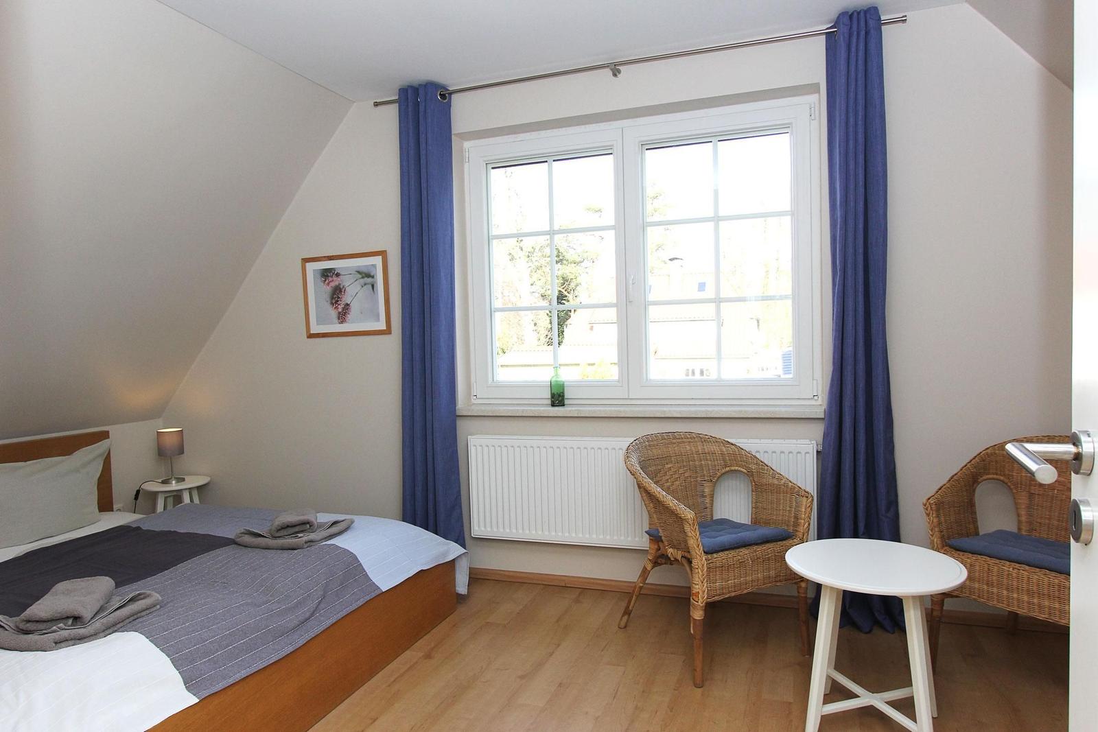 Schlafzimmer mit Dachschräge, Bett, zwei Stühlen und Fenster mit Vorhängen.