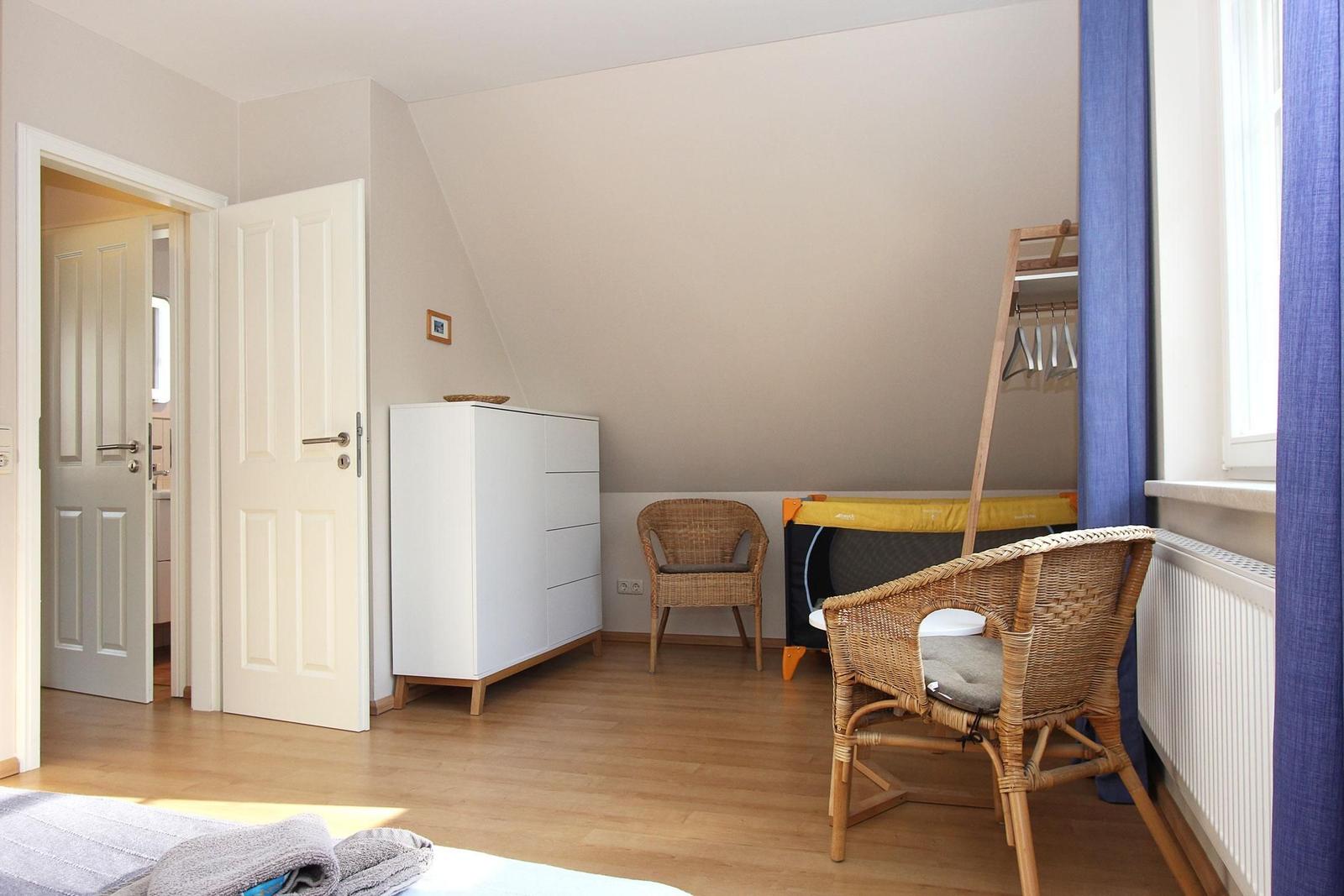 Zimmer mit Holzboden, weißen Türen, Wickerstühlen und Kleiderschrank.